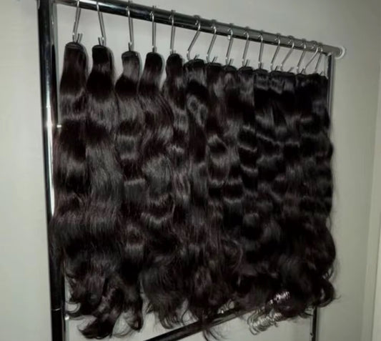 Collection of black hair extensions on a metal rack against a white wall.